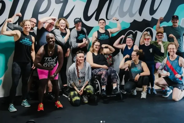 A group of adaptive athletes and trainers flexing together in front of a gym mural