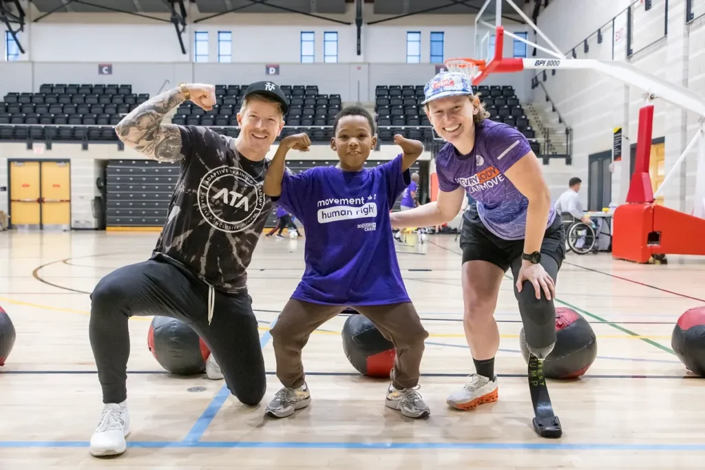 ATA co-founder Logan Aldridge flexes alongside a young athlete with an upper-limb difference and a trainer with a leg prosthesis