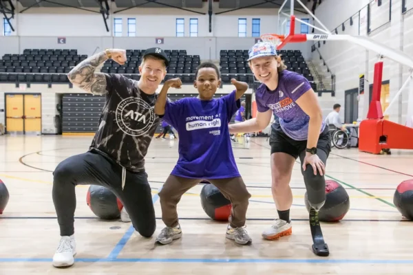 ATA co-founder Logan Aldridge flexes alongside a young athlete with an upper-limb difference and a trainer with a leg prosthesis