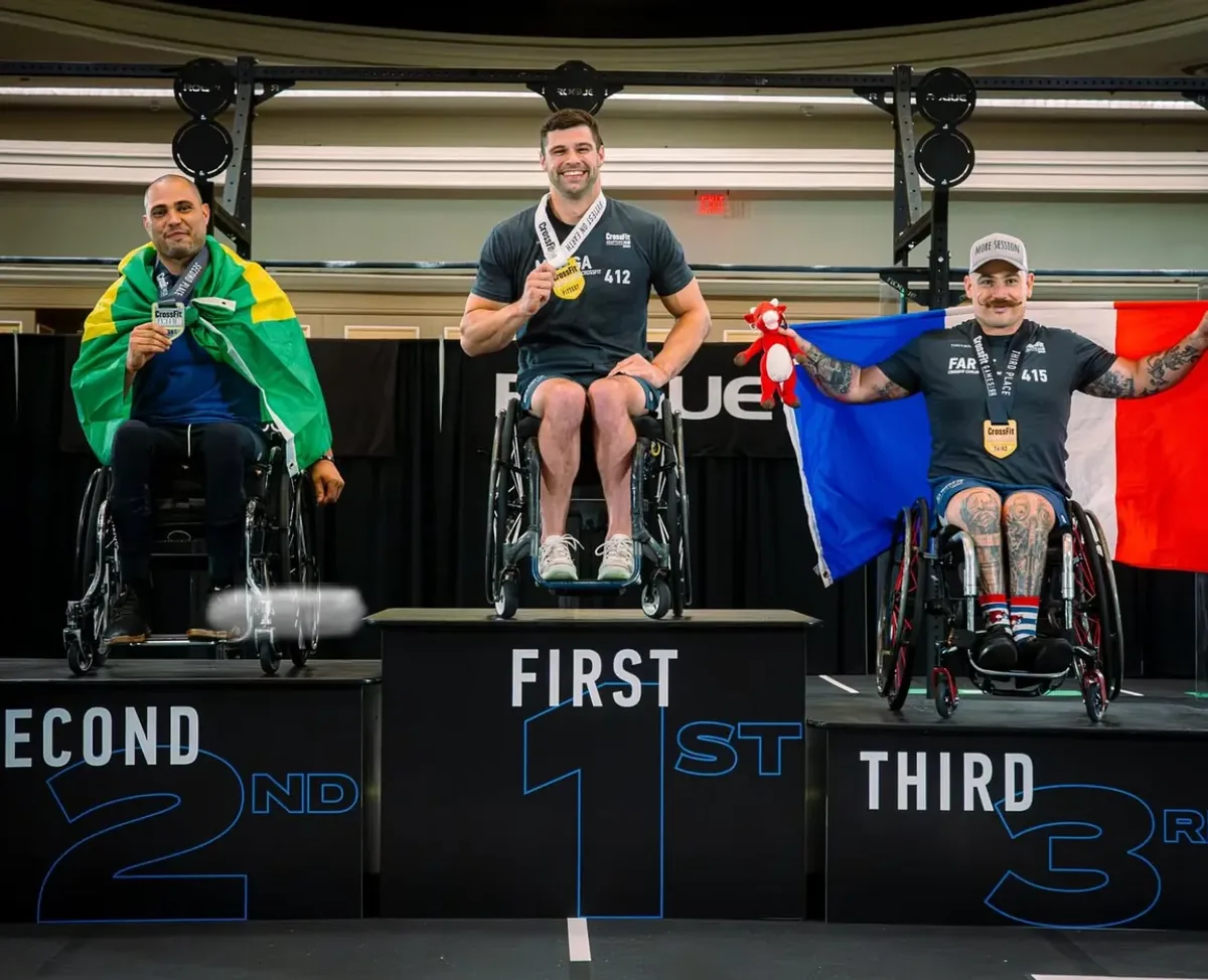 Tom Miazga on the top step of the CrossFit Games adaptive division podium beside the second and third place athletes