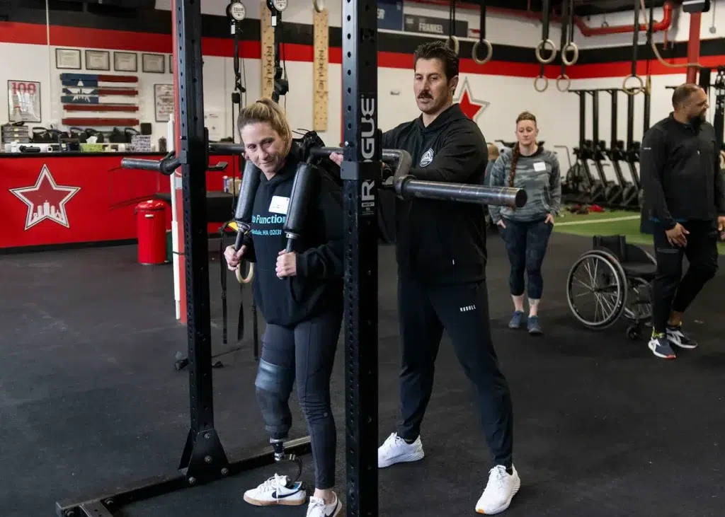A trainer coaches an athlete with a leg prosthesis at a squat rack
