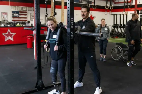 A trainer coaches an athlete with a leg prosthesis at a squat rack